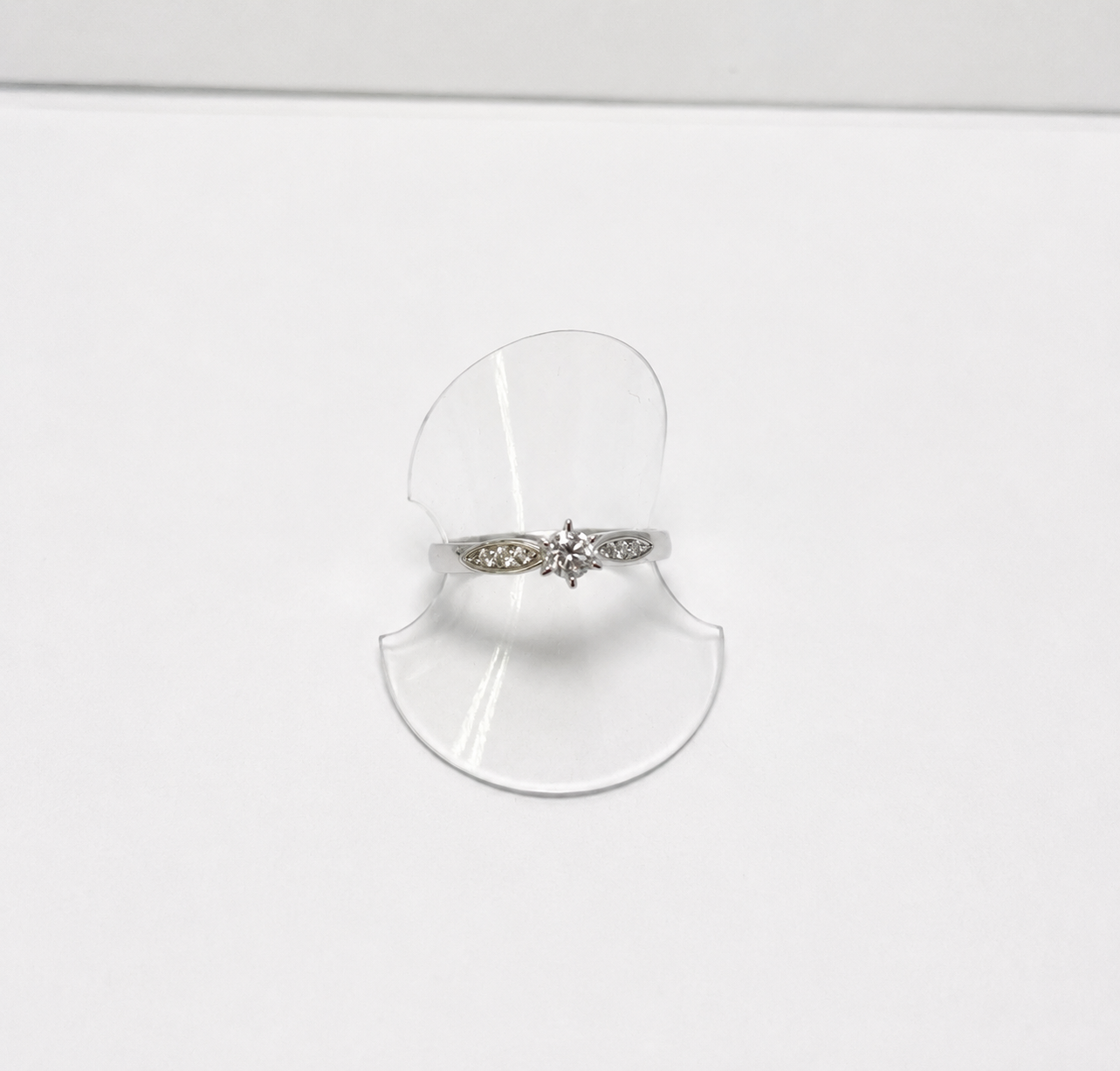Silver ring with a decorative band on a clear stand against a white background