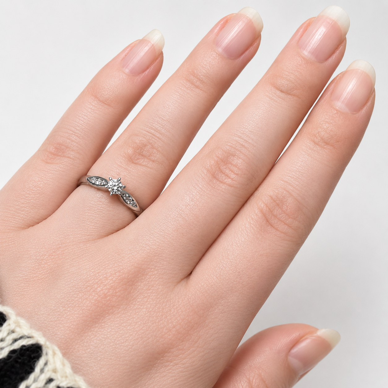 Hand wearing a silver ring with a diamond on a neutral background