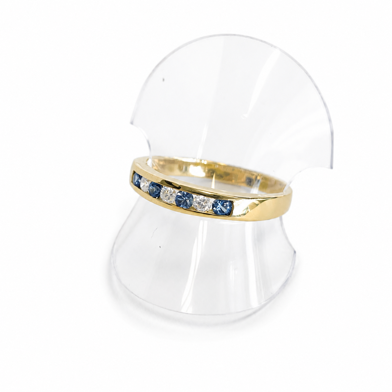 Gold ring with blue gemstones on a clear stand against a white background