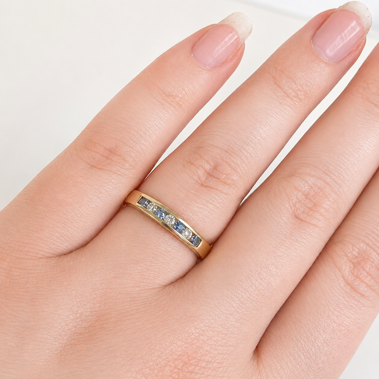 Gold ring with blue gemstones on a hand against a white background