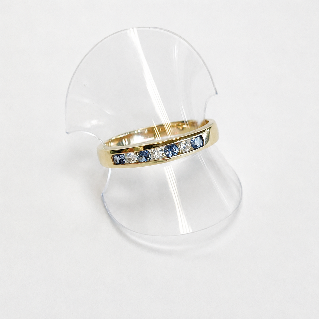 Gold ring with blue and clear stones on a clear stand against a white background