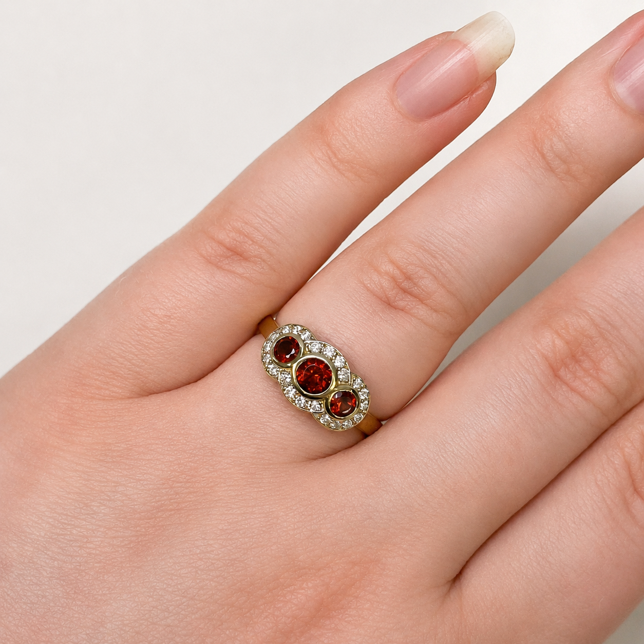 Gold ring with red gemstones on a hand against a neutral background