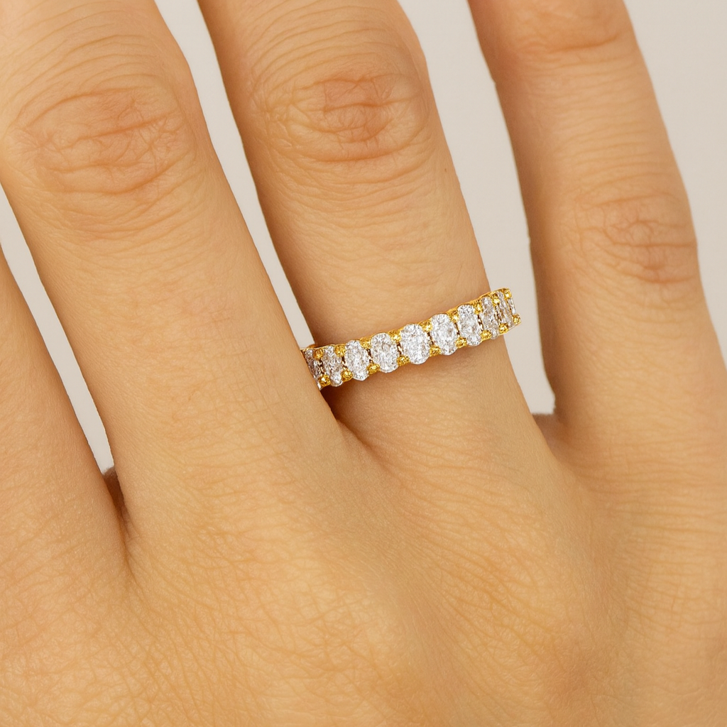 Gold ring with diamonds on a hand against a neutral background