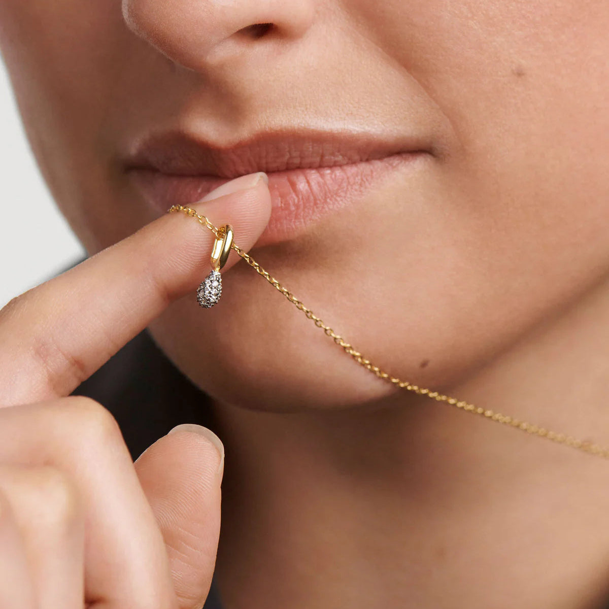Close-up of a gold necklace being worn and adjusted by a person.