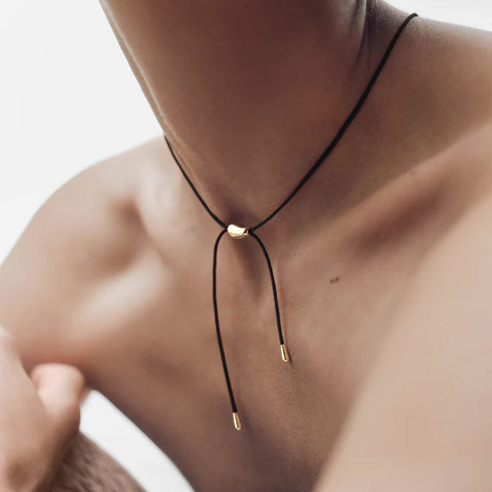 Close-up of a person wearing a black cord necklace with gold accents.