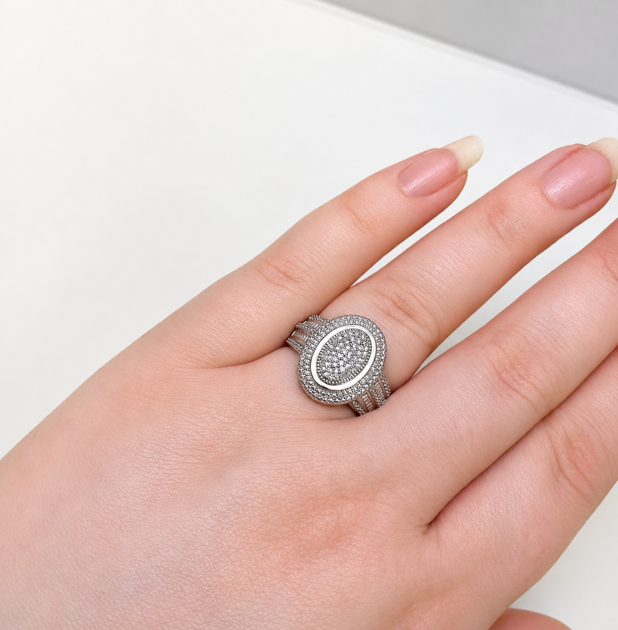 Silver ring with gemstones on a hand against a light background