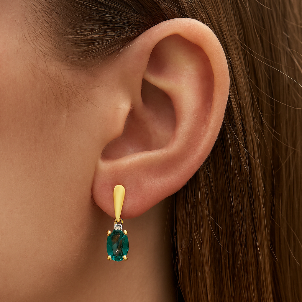 Close-up of an ear wearing a gold earring with a green gemstone.