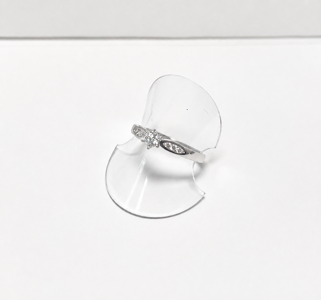 Silver ring with a bow on a clear stand against a white background
