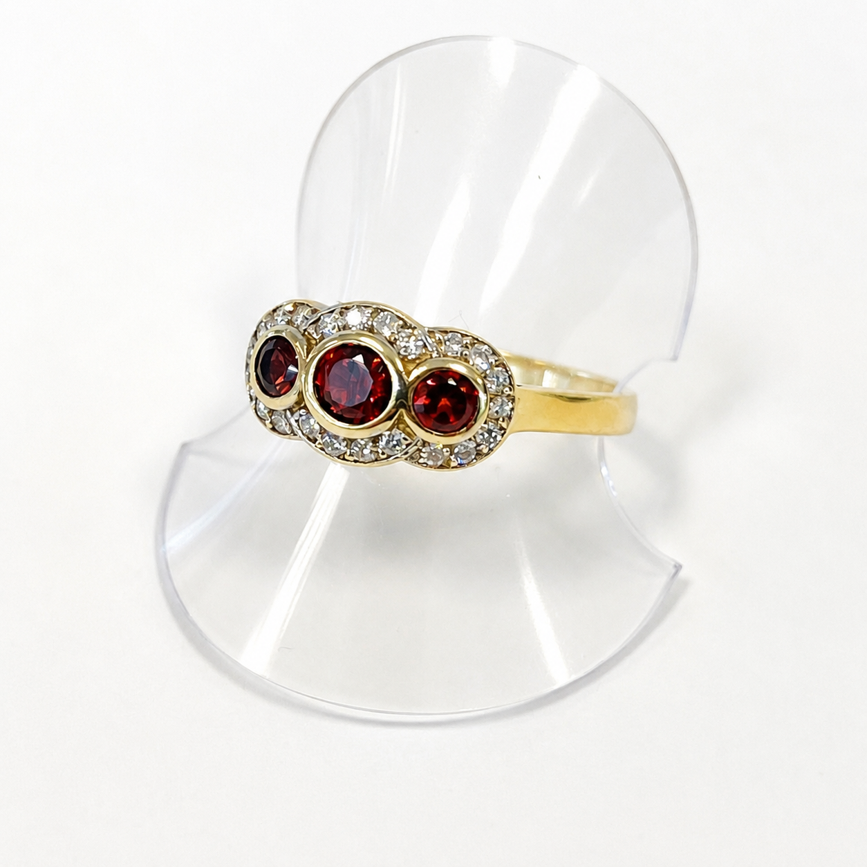 Gold ring with red gemstones on a clear stand against a white background