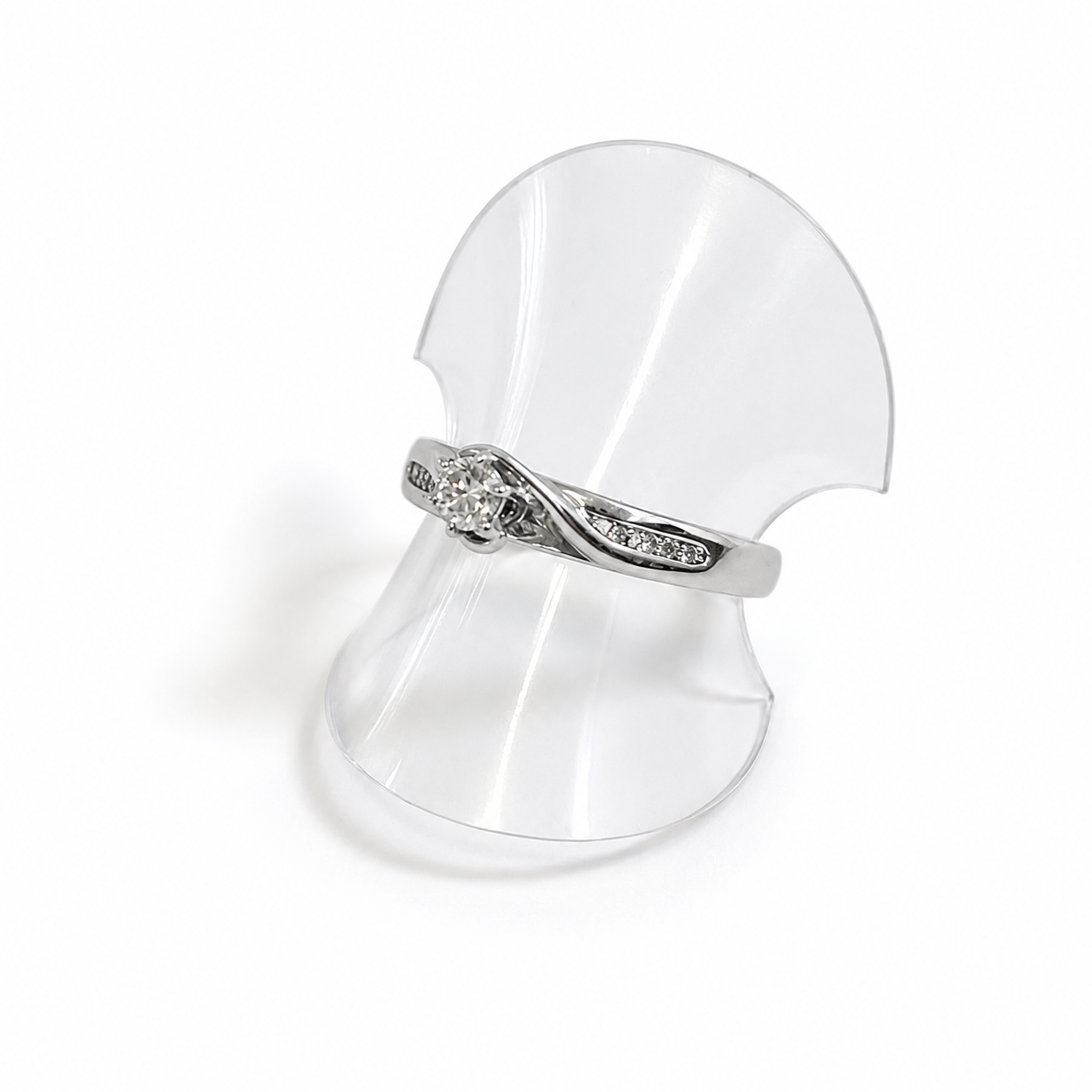 White gold ring with a diamond on a clear plastic stand against a white background